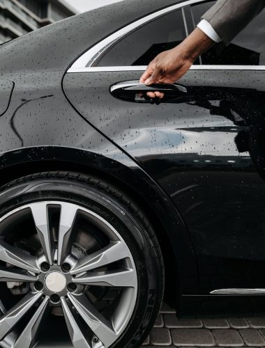 Close-up of a hand opening a black luxury car door on a rainy day. Elegant and modern design.